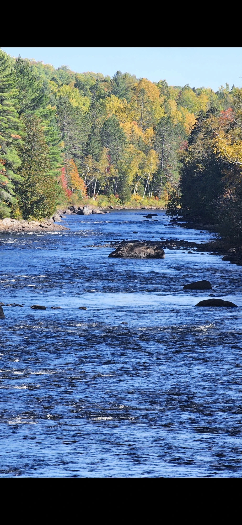 Find the seam: fast water sliding past the calm pocket behind the boulders